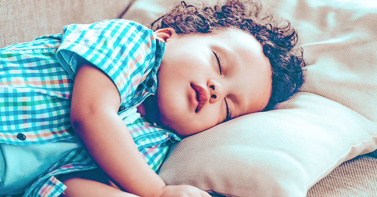 a toddler boy wearing a blue shirt laying on a tan couch pillow