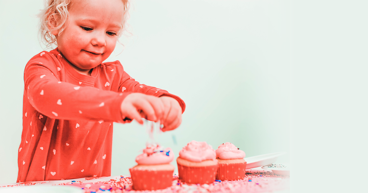 little girl in red shirt decorating valentines day cupcakes